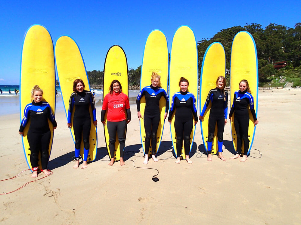 Learning to surf class stand in the sand in front of their yellow boards