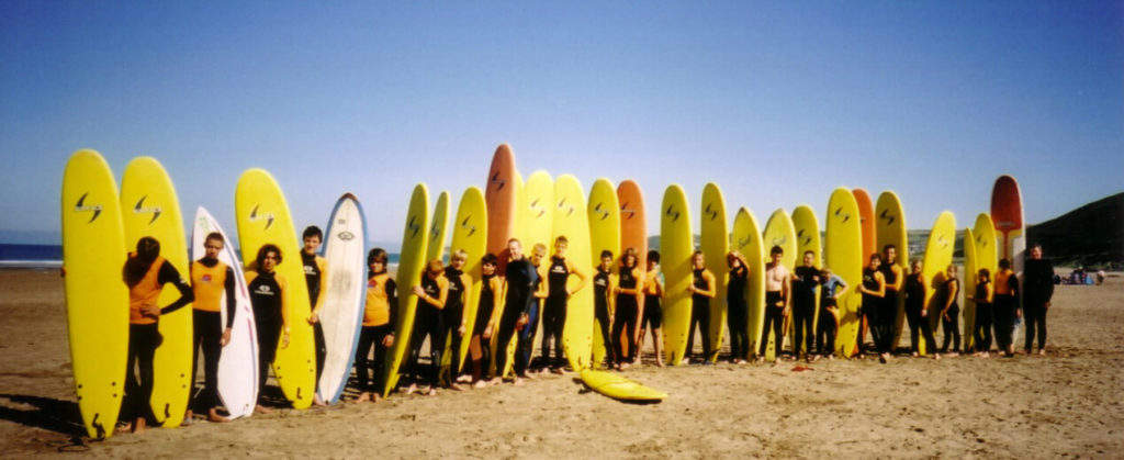 Large group of people with yellow surf boards lined up in a row for surfing lessons