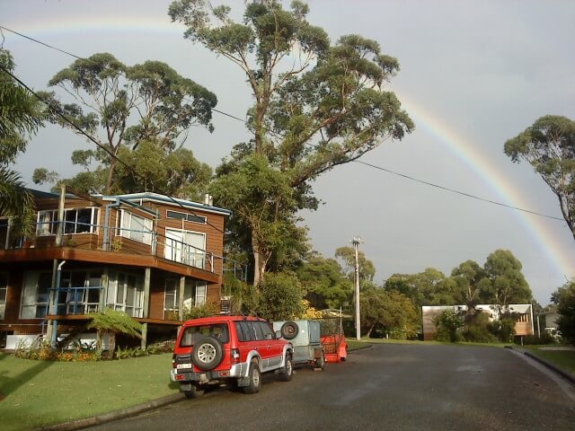 house beside a road with rainbow in sky in the background