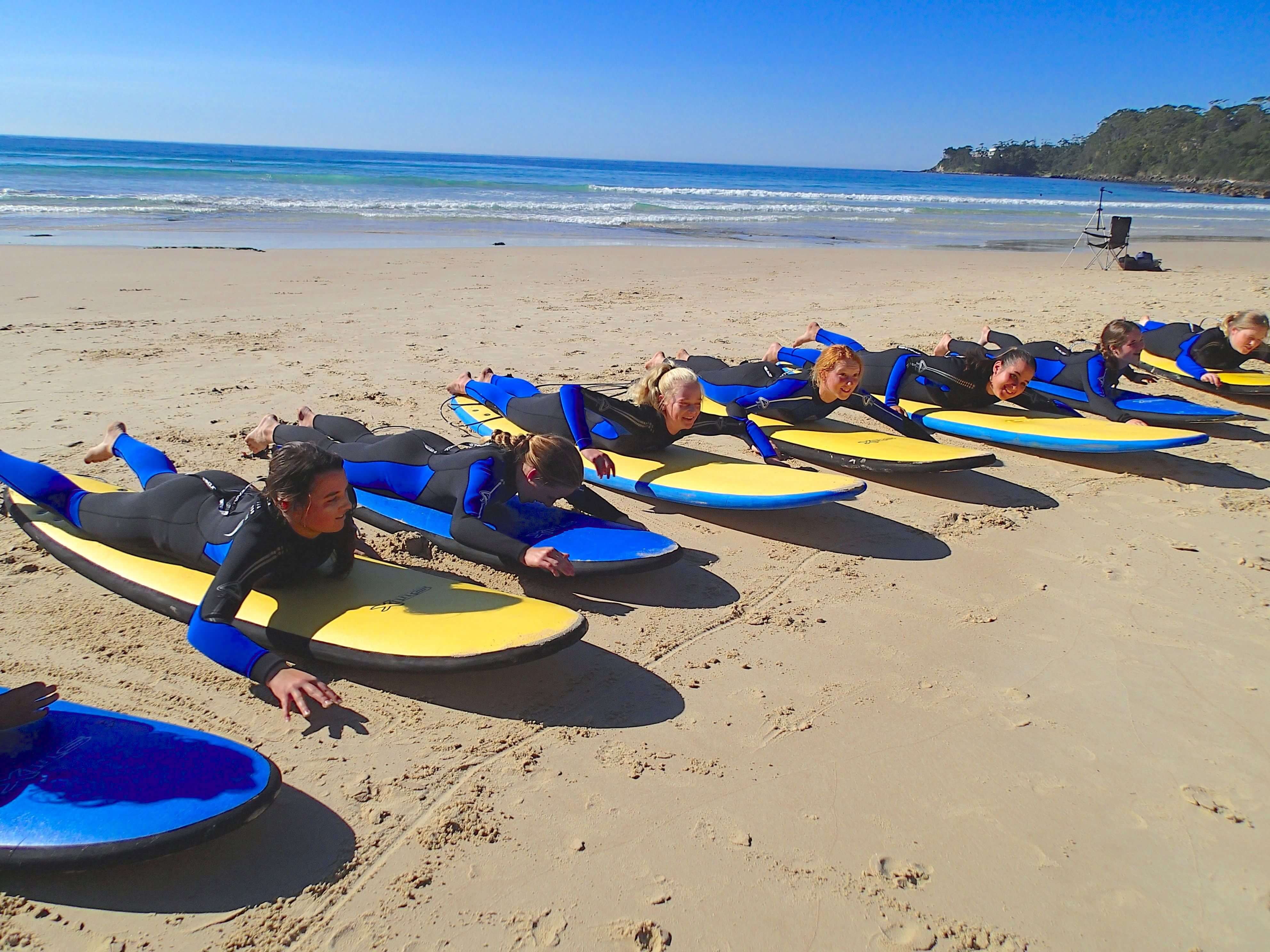 Learn to suf class participant laying on their surf boards on the sand