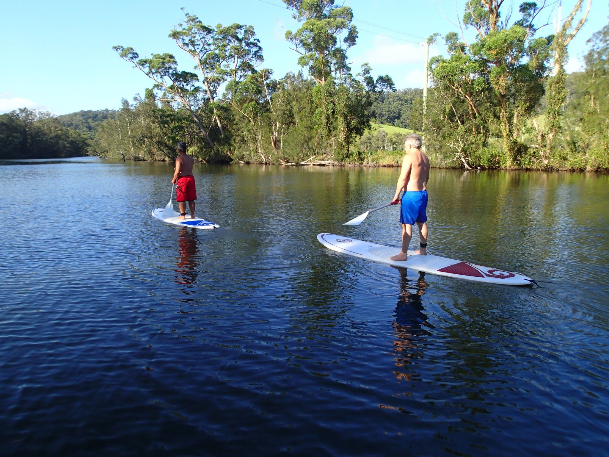 wide shot of men standing up on paddle boards on the water