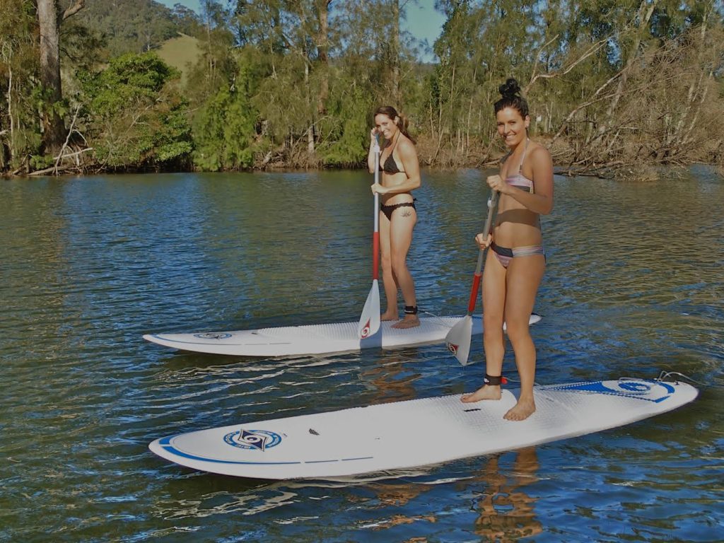 Smiling women standing on paddle boards on water