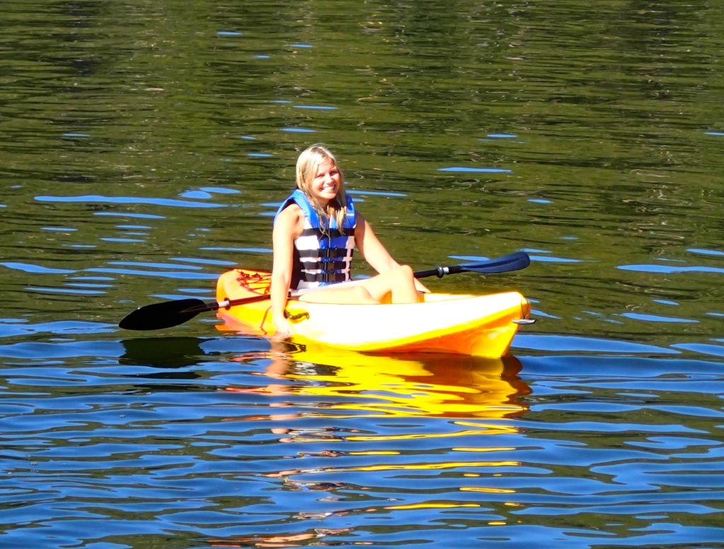 Girl smiling with life jacket on in yellow kayak on the water