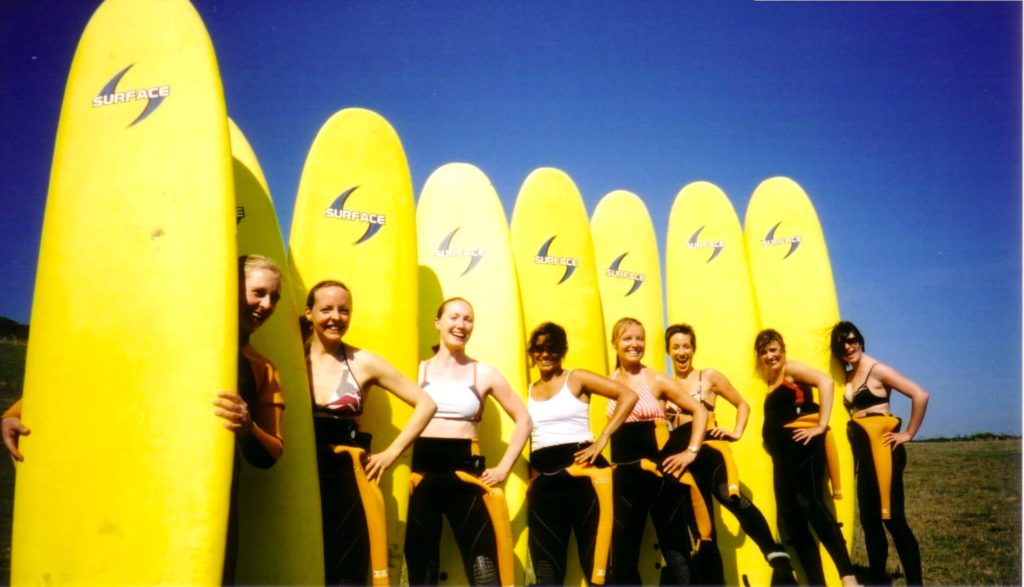 Smiling women standing beside their yellow surf boards with very blue sky in the background