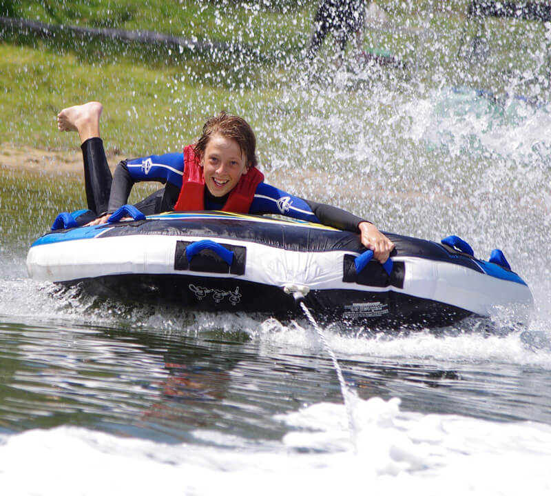 Action shot smiling child in wetsuit and life jacket laying down on wake board