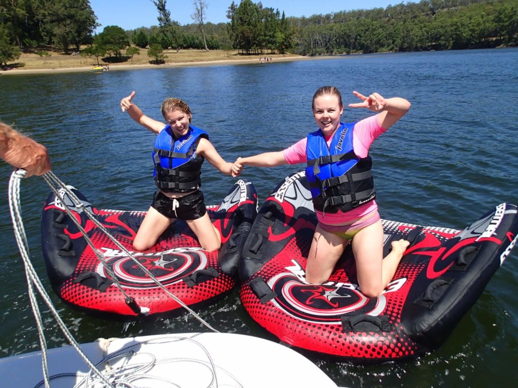 Smiling girls posing in life jackets on wake boards on the water