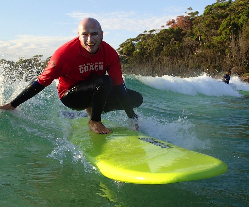 WOW & Ulladulla Surf Schools' Head Coach surfing on yellow surfboard with hand stretched out touching the water