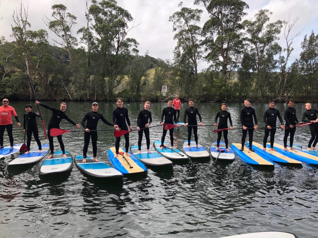 Group posing for photo standing on paddle boards with paddles in their hands on the water