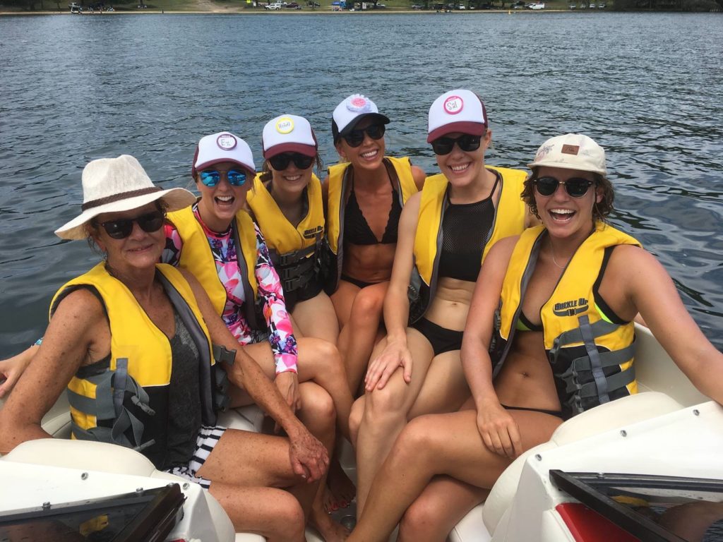 Smiling female group with yellow life jackets sitting together in a boat on the water