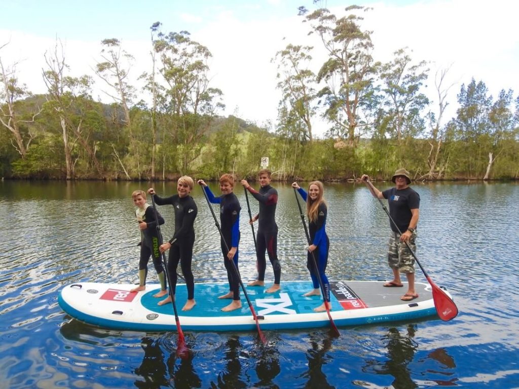 Smiling group of children with coach standing on paddle board paddling on water