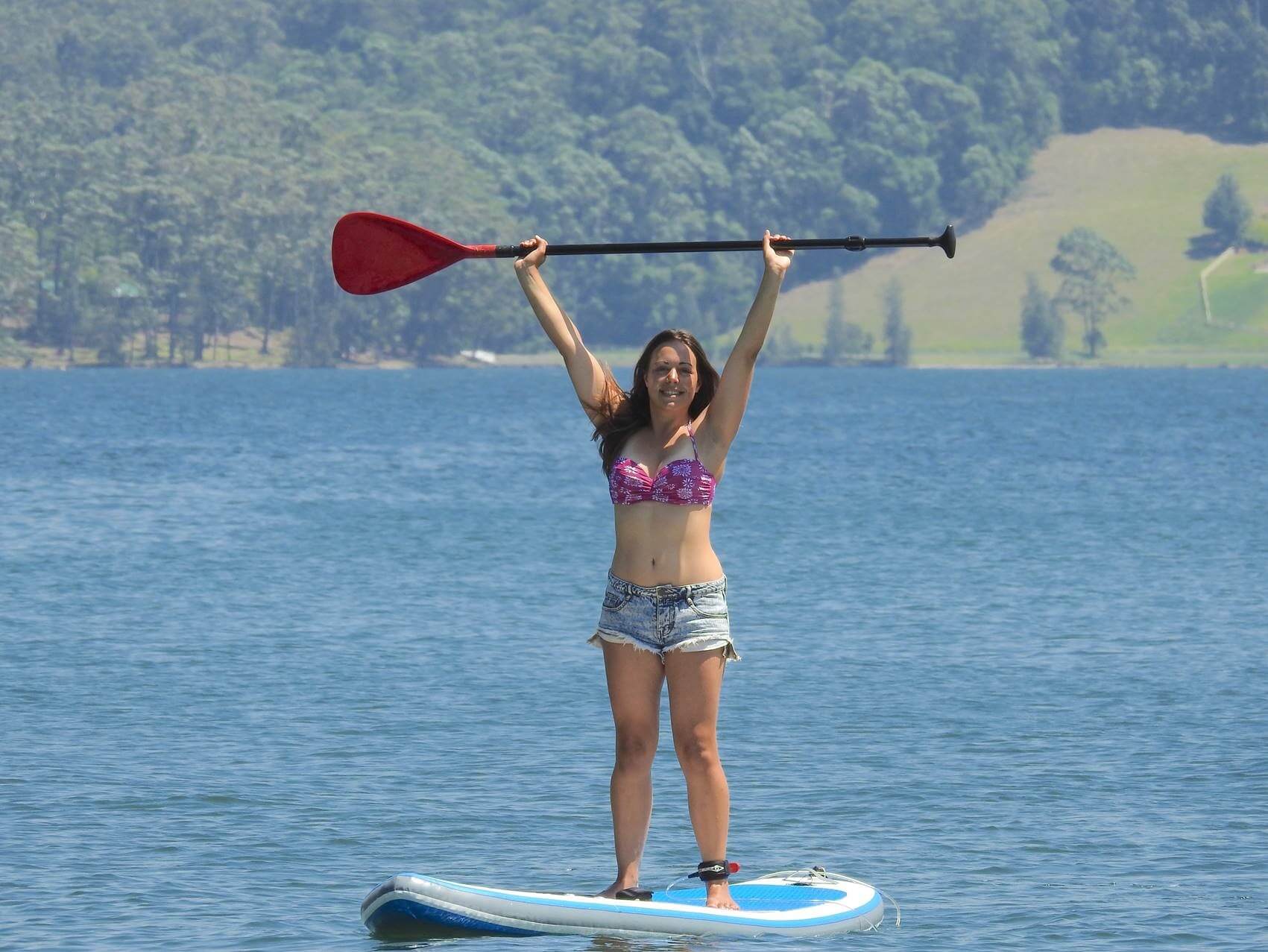Women standing on paddle board on the water holding paddle with both hands above her head