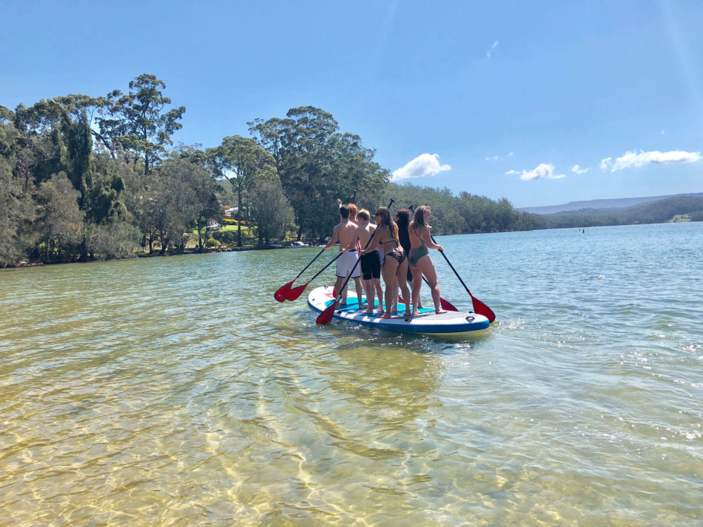 Party group standing on paddle board paddling on water