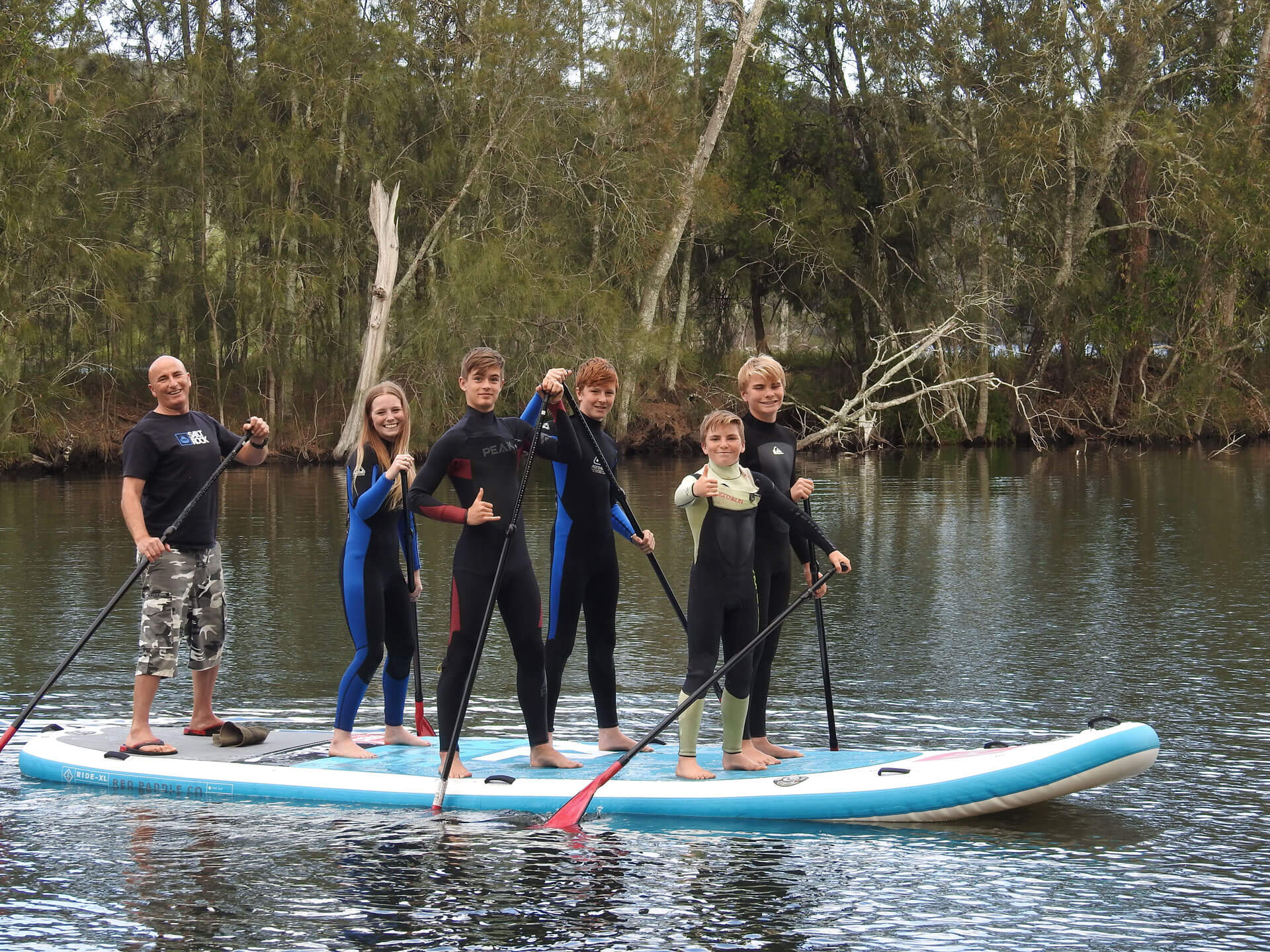 Group of smiling children and coach standing on monster paddle board on the water