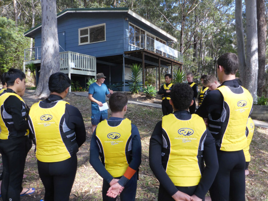 Group of people listening to surf lessons and water course coach with blue house in the background