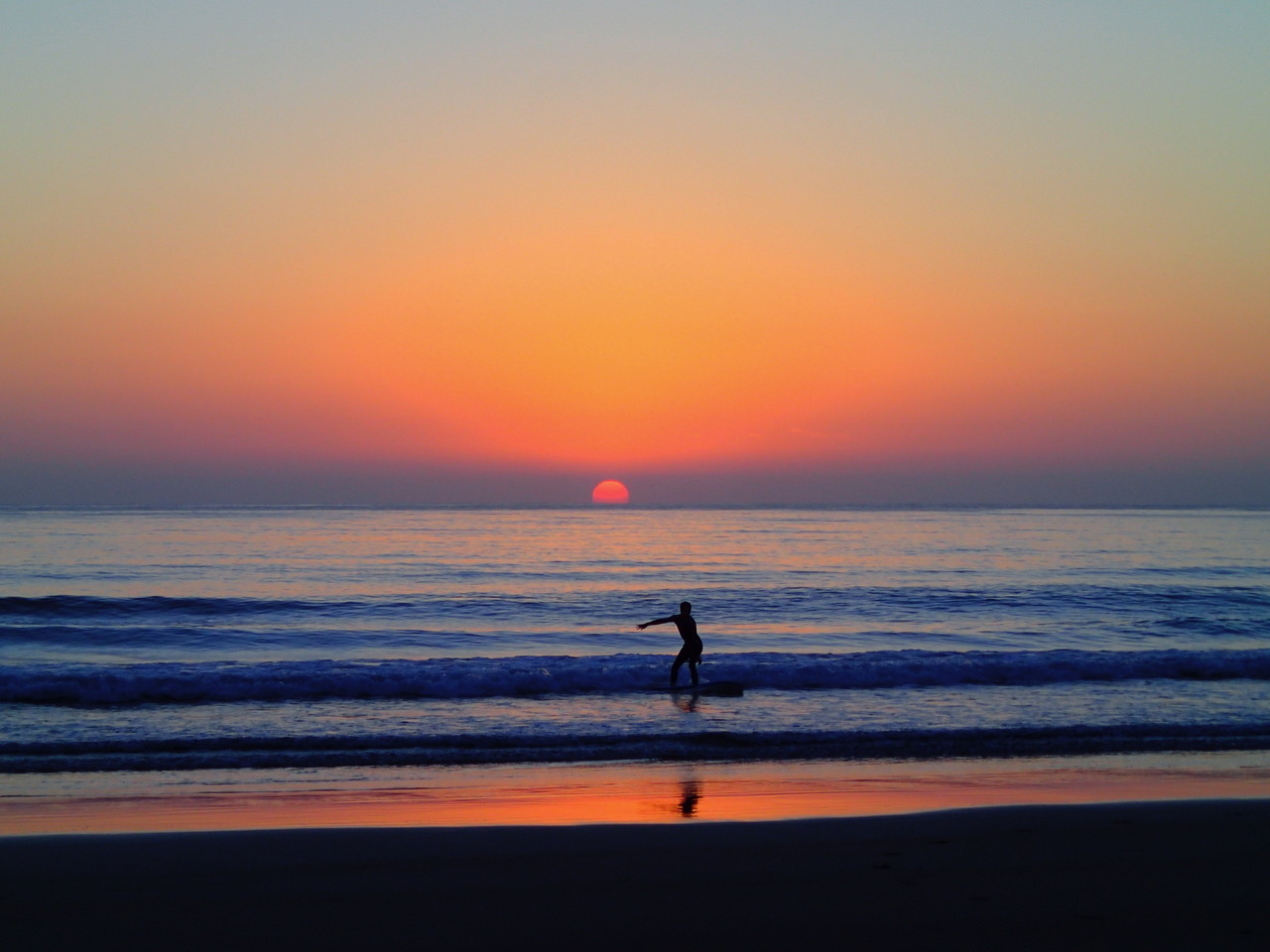 Beautiful sunset over the ocean with silhouette of person standing on surfboard riding a wave