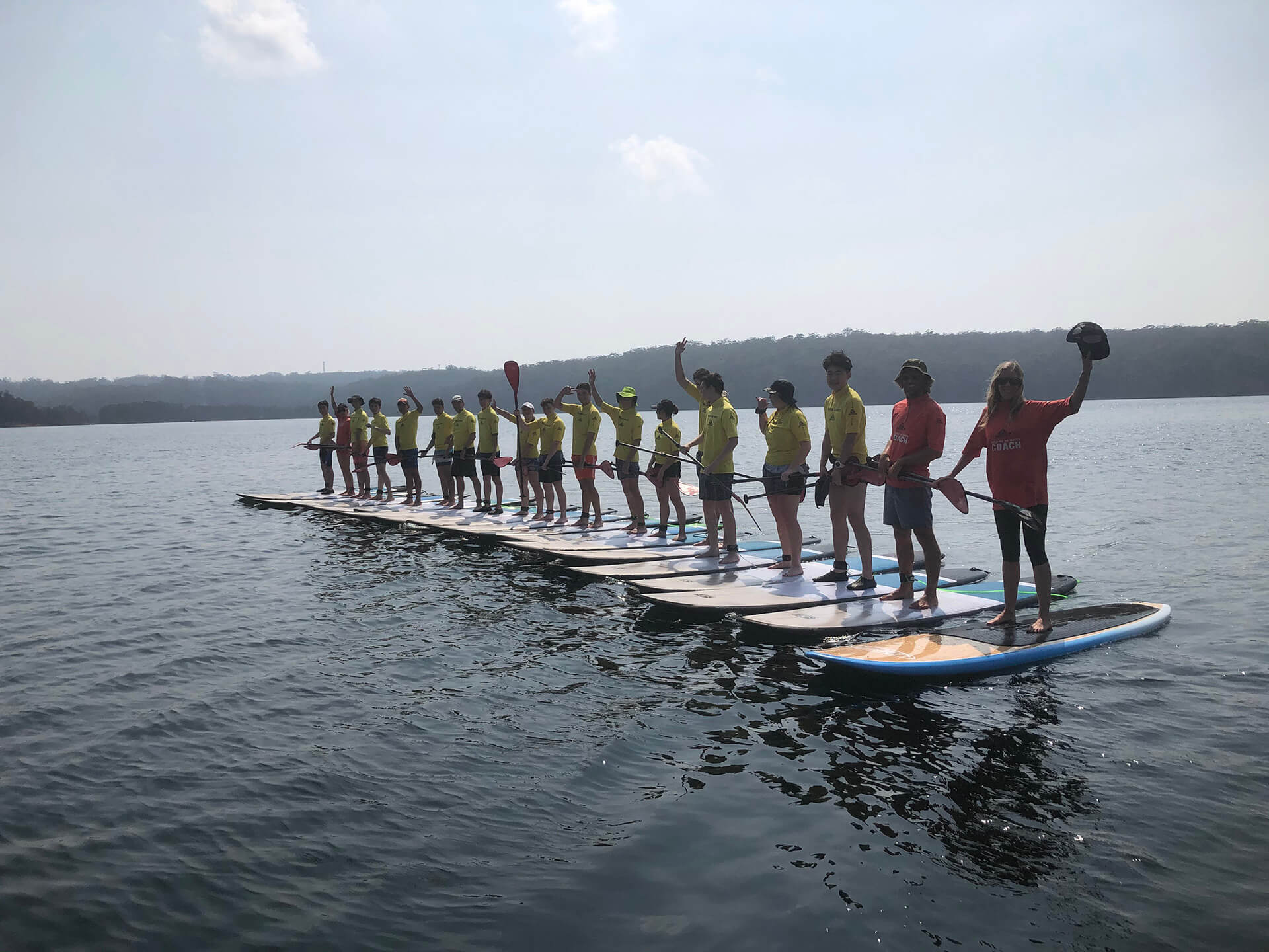 Waving people standing up on paddle boards in the water in a row