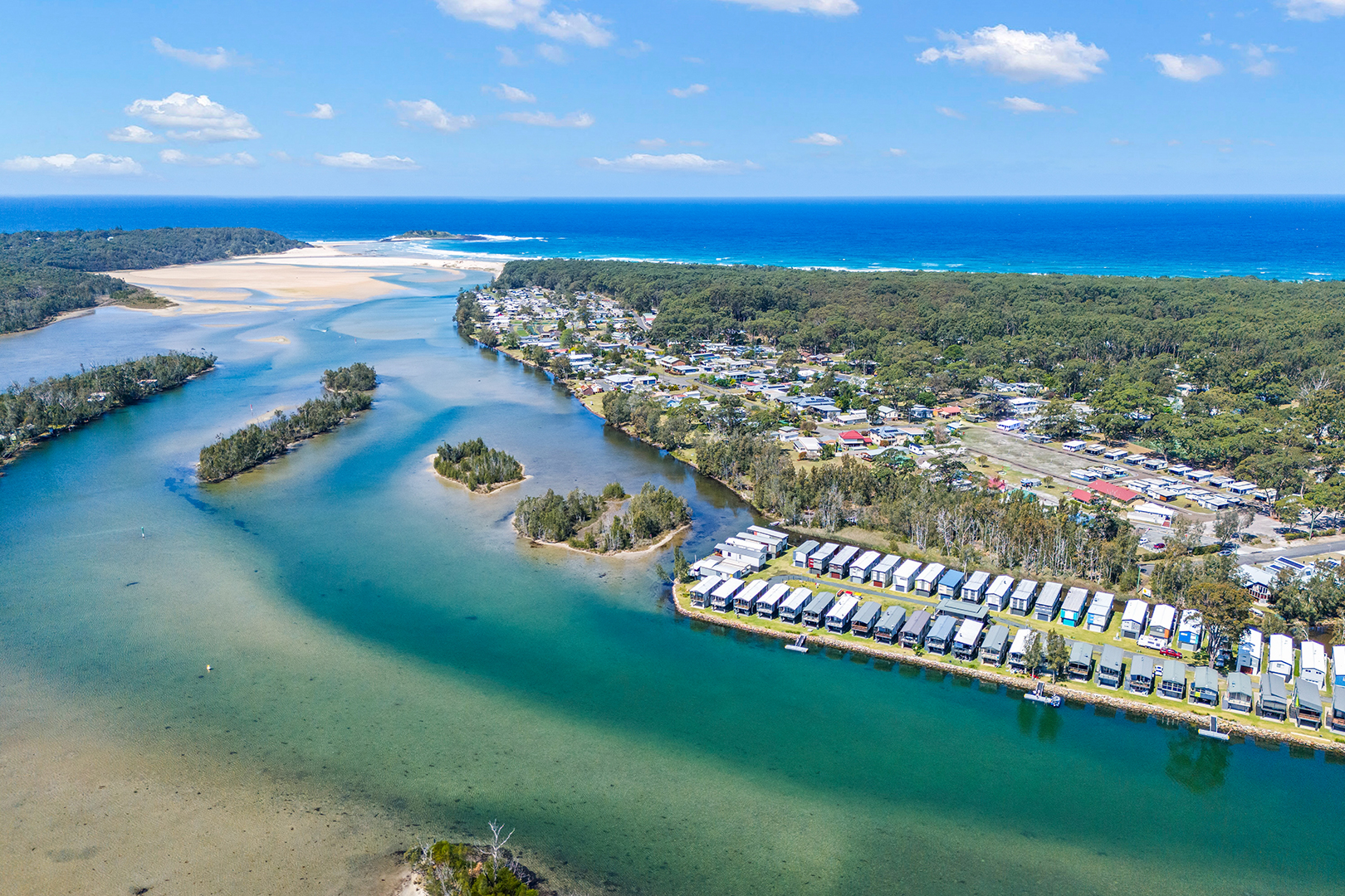 Scenic aerial photograph of Lake Conjola showing pristine waterways, small islands, waterfront residential community, surrounding bushland, and pristine beaches meeting the Pacific Ocean - ideal location for watersports and recreational activities